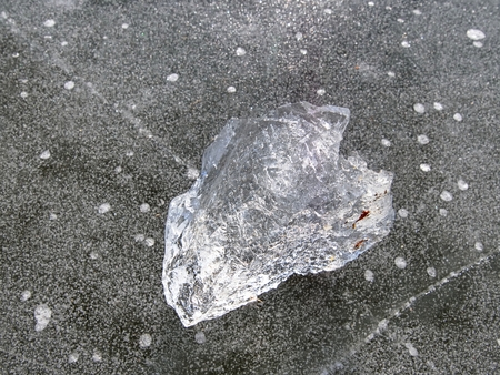 Transparent ice piece on the lake. Crystal clear piece of ice squeezed the lake, sun rays create...