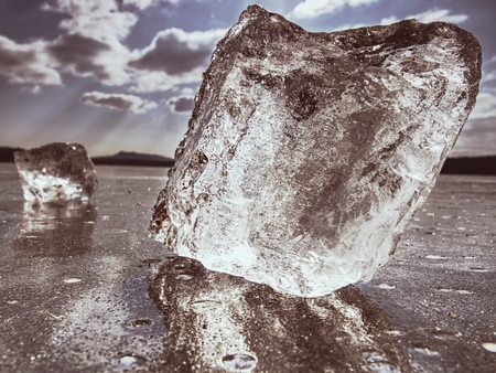 Transparent ice piece on the lake. Crystal clear piece of ice squeezed the lake, sun rays create...