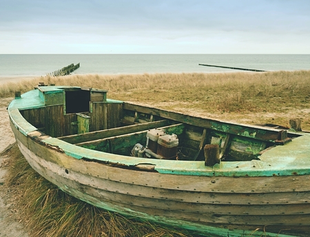 Wrecked fishing boat on old dry grass. Abandoned wooden ship with damaged engine stay on sandy dune far from sea..の写真素材