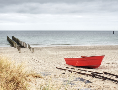 Abandoned fishing paddle boat on sandy beach. Quiet sea water level during morning windless.の写真素材