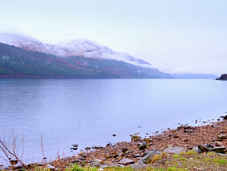 Smooth lake with high cone mountains and hidden snowy peaksの写真素材