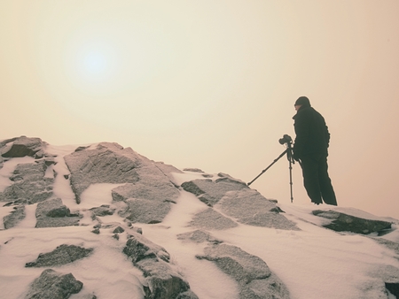 Travel photographer doing pictures in ancient stones on snowy peak of mountain. Winter cold and misty morning in mountainsの写真素材