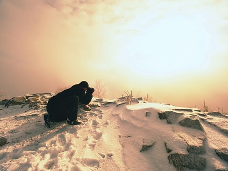 Photographer lay in snow on mountain peak and takes a picture of fantastic landscape around, snowy winter dayの写真素材