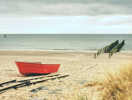 Abandoned red paddle boat on sandy beach of sea.  Smooth water level within morning windless. Dramatic and picturesque scene. の写真素材