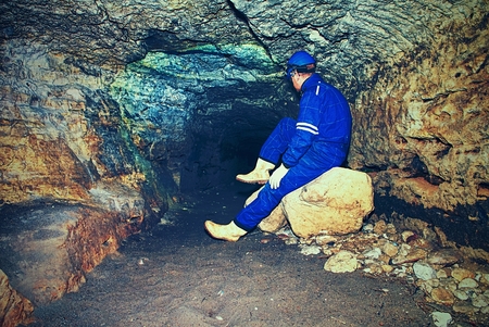 Site contractor engineer in blue overal, rubber boots and protective helmet in subterranean tunnel. The specialist checks the quality of the subsoil beneath the city.の写真素材