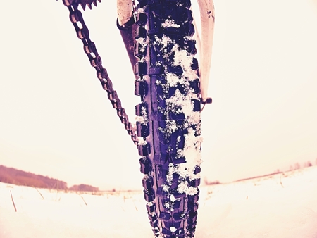 Rear wheel detail of mtb. Snow flakes melting on dark off road tyre. Winter weather in the field.