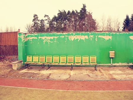 Vintage steel seats on outdoor stadium players bench chairs with worn paint below green wallの写真素材