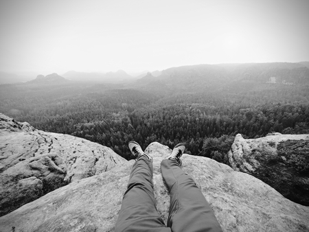 Legs of traveler on high mountain top in travel. Leather trekking shoes on peak of rock above misty valley.  Freedom conceptの写真素材