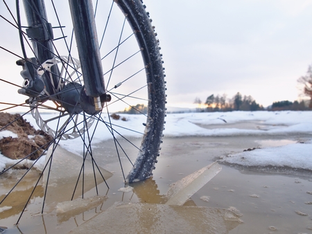 Bike drowned in muddy pool within winter trip. Broken pieces of ice around freeze terain tyre, wide viewの写真素材