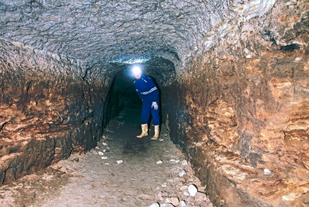 Underground work. Hunched worker in a blue overall and a safety helmet stands in the underground...