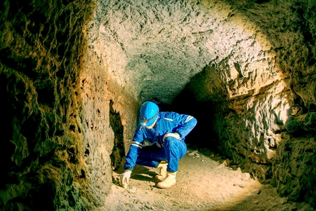 Man works in the mystical ancient tunnel from orange sandstone walls, city underground. Interiors of castle catacombs, view through the stone tunnelの写真素材