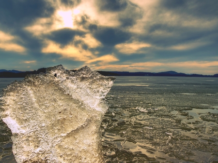 Ice melting on sandy beach. Close-up of ice floe with deep cracks inside. The end of crue winter coming.の写真素材