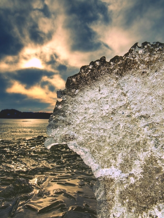Icy sheets melting on sandy beach. End of long and crue winter coming. Detail of ice floe with deep...