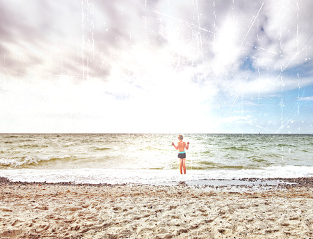 Abstract effect. Blond hair on a white background. Kid on stony beach with foamy waves. Windy day, cloudy blue sky on seascapeの写真素材