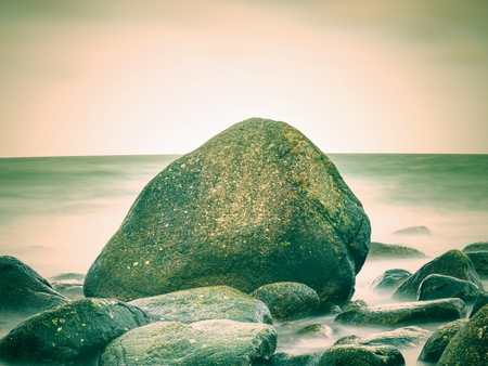 Romantic morning at sea. Big boulders sticking out from smooth wavy sea. Pink horizon with first hot sun rays. Vintage Style effectの写真素材