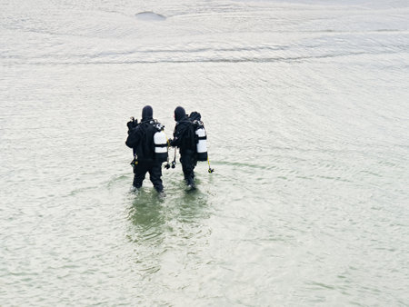 Prerow Germany - January 25 2018: Two winter scuba divers walking with their gear in shallow water towards to the beach.のeditorial素材