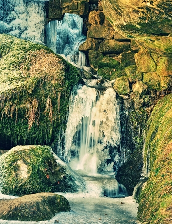 Winter frozen waterfall. Small pond and snowy boulders bellow cascade of waterfall. Crystal freeze water of mountain river and sounds of falling water.の写真素材
