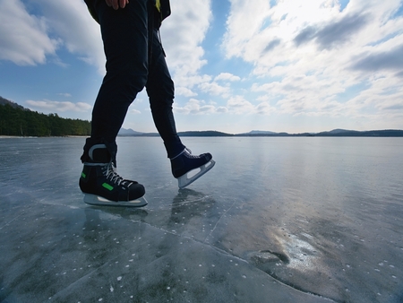 Man ice skating on frozen lake. Thin ice with deeep cracks below man legs.の写真素材