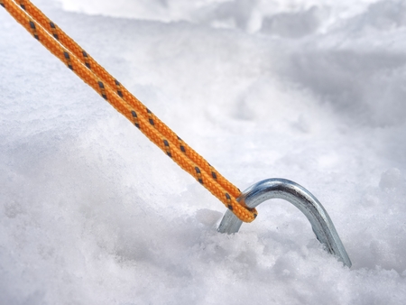 Detail of tent nylon strap anchored into snow.  Camping in wild nature park in early spring. Adventure travel active lifestyle freedom outdoors.の写真素材