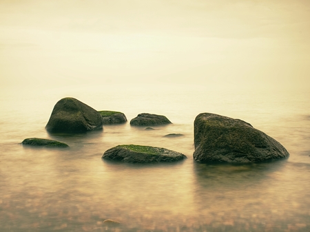 Stony coast defies to waves of ocean clear sky with blurred Sun in high humidity. Smooth evening Sea between stones and horizon. Peaceful Background with Tranquil Calm Water.の写真素材