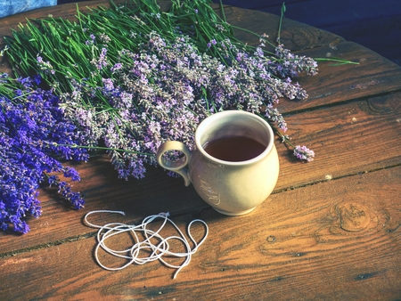Aroma designer  workplace. Girl prepar harvested lavander stalks for drying. Rustic wooden tble with cup of herbal teaの写真素材