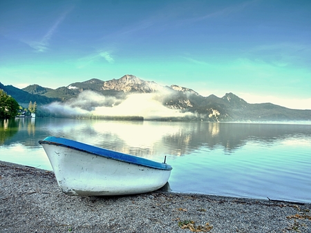 Abandoned fishing boat on bank of Alps lake. Morning lake glowing by sunlight.の写真素材