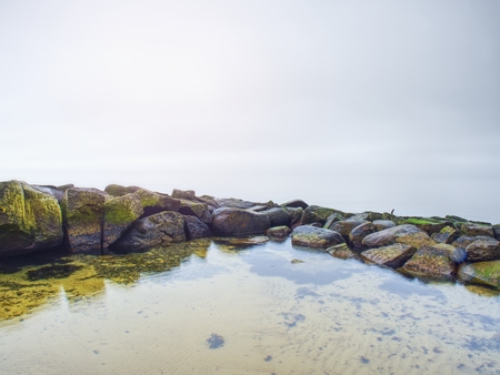 Stony coast defies to waves of ocean clear sky with blurred Sun in high humidity. Smooth evening Sea between stones and horizon. Peaceful Background with Tranquil Calm Water.の写真素材