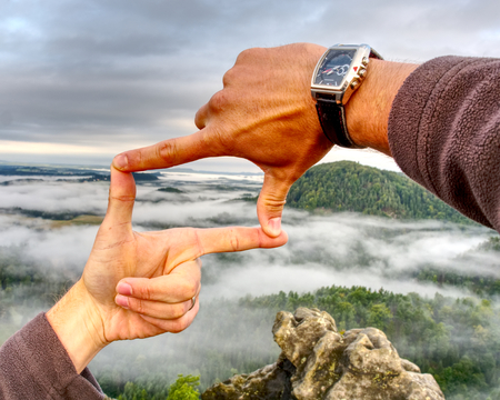 Frame made of hands and nature landscape. Palms with fingers making a frame sign over misty landscapeの写真素材