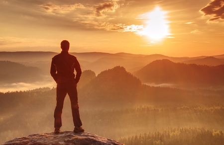 Handsome athletic man, a tourist, stay on summit rock. Wild misty mountain landscape.の写真素材
