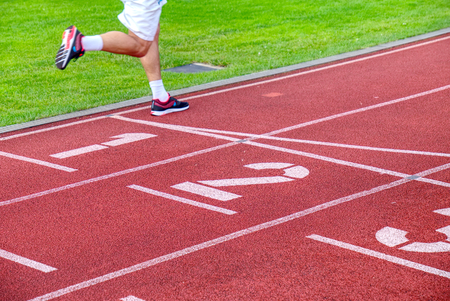 Running legs and moving shadow of a male athlete running on track of outside stadium.の写真素材