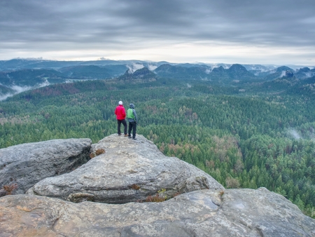 Friends in nature. Tourists travelers with backpacks in the rocks watch the landscape in mist. Poor visibilityの写真素材