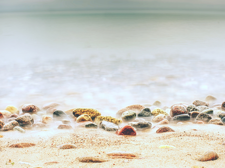 Rounded colorful pebbles on a beach, tide up commingの写真素材