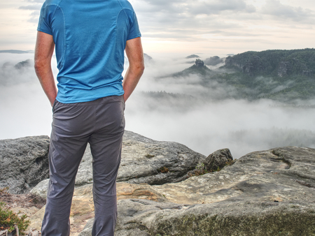 Gloomy nostalgic view into fall nature with lonely melancholic adult man. Sportsman without jacket standing on top in misty morning and thinkingの写真素材
