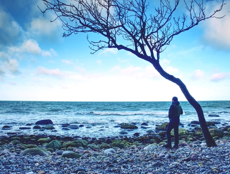 Tourist figure stand on rocky stony coast. Sun beams make reflection in salt waterの写真素材