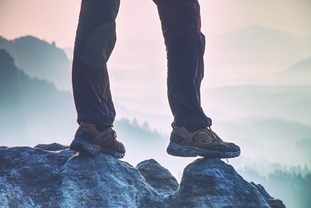 Feets and legs of hiker on peak with hiking trail and misty mountain range background. Nature with misty cap at sunriseの写真素材