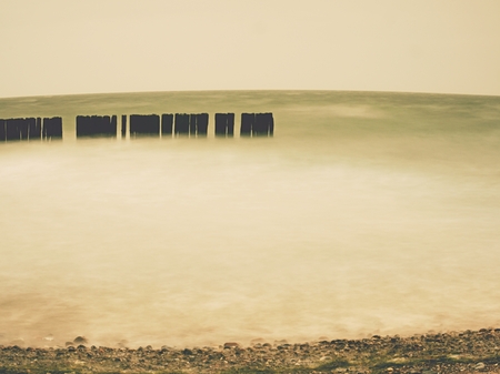 Seascape with breakwaters at sunset with foamy waves on beach and heavy cloud coverの写真素材