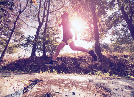 Male runner is jumping during outdoors training for marathon run in park. Fit young sport fitness model outdoor.の写真素材