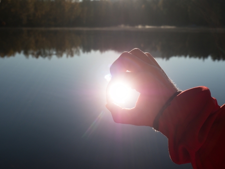 Hands stretch toward the sun on lake level.  Just look at the sunset through the folded fingersの写真素材