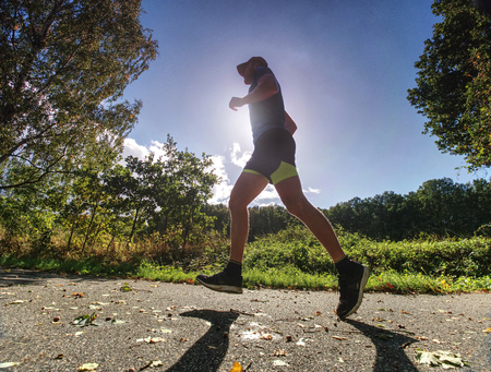 Man running on asphalt track. Athlete running fast in a park with dense trees in the background.の写真素材