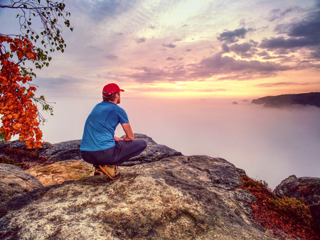 Hiker in middle of nowhere and thinking alone. Man sit on top of a sharp peak enjoying sunrise.の写真素材