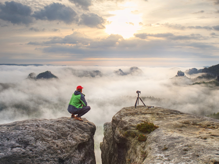 Photographer or videographer traveler thinking close to tripod with digital camera prepared for an art work. Colorful fall in wild natureの写真素材