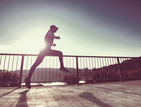 Man is training in the nature with sun behind him. Young man on morning run outdoors.の写真素材