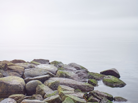 Ocean waves crashing on rocky breakwater. Calm evening sea level and strongly enlightened stones...