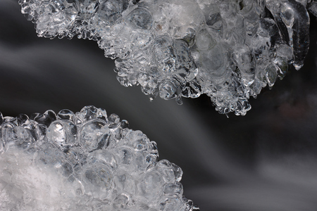 Winter creek with icicles above freeze stream. Detail of frozen brook - small waterfall stone icicles and milky streamの写真素材