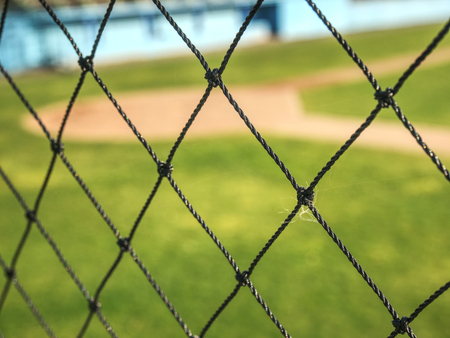 Empty baseball green field view grandstand.  View through safety net around baseball field on sunny...