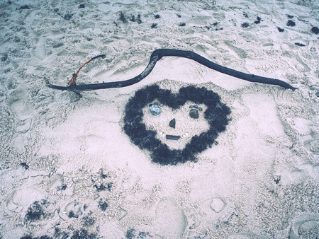 Face in beach sand. Children created heart made of brown water algae and stones.の写真素材