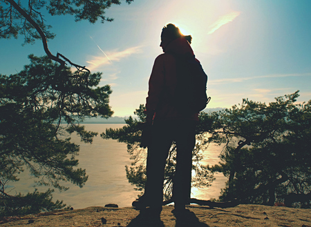Silhouette of winter clothed woman walking at icy lake in sunset
