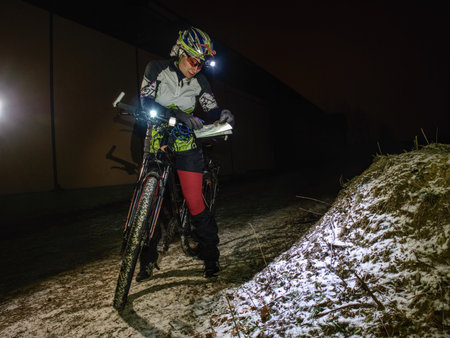 Outdoor orienteering extreme bike race in night. January 25th 2019, Novy Bor, Czech Republic. Woman check the map. Kind of sports that require navigational skills using a map and compass to achieve target.のeditorial素材