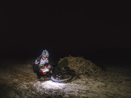 Outdoor orienteering extreme bike race in night. January 25th 2019, Novy Bor, Czech Republic. Woman check the map. Kind of sports that require navigational skills using a map and compass to achieve target.のeditorial素材