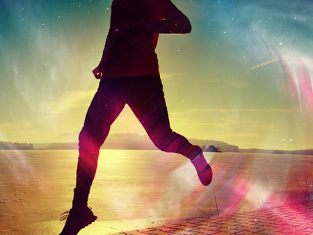 Silhouette of runner person running along on the beach at sunset with sun in the background. Vintage effect style pictures.の写真素材